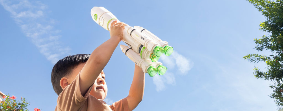 Child playing with a toy rocket against a clear blue sky