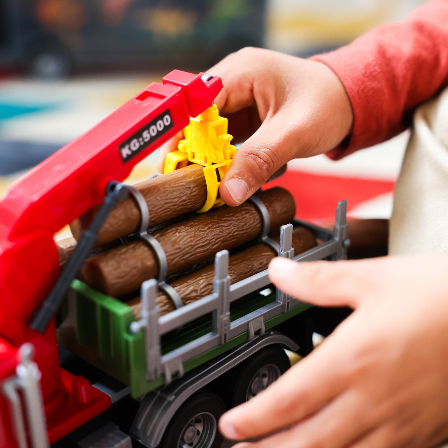 A close-up of a child's hands playing with a toy logging truck. 