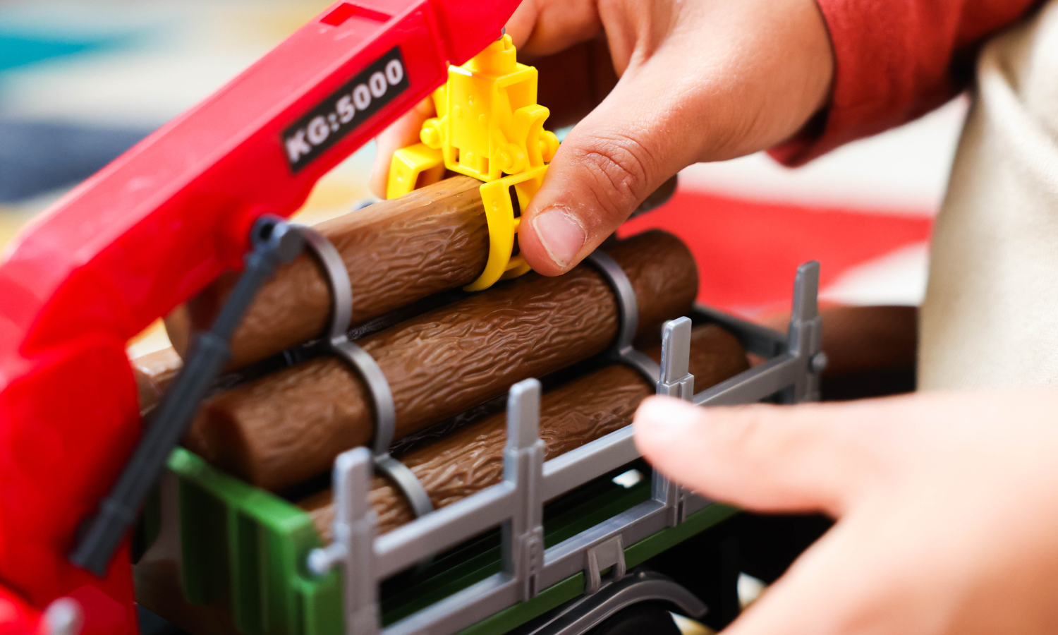 A close-up of a child's hands playing with a toy logging truck. 