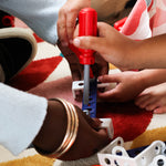 A close-up lifestyle shot of multiple hands using a red-handled screwdriver to assemble white plastic building pieces on a colorful patterned rug.