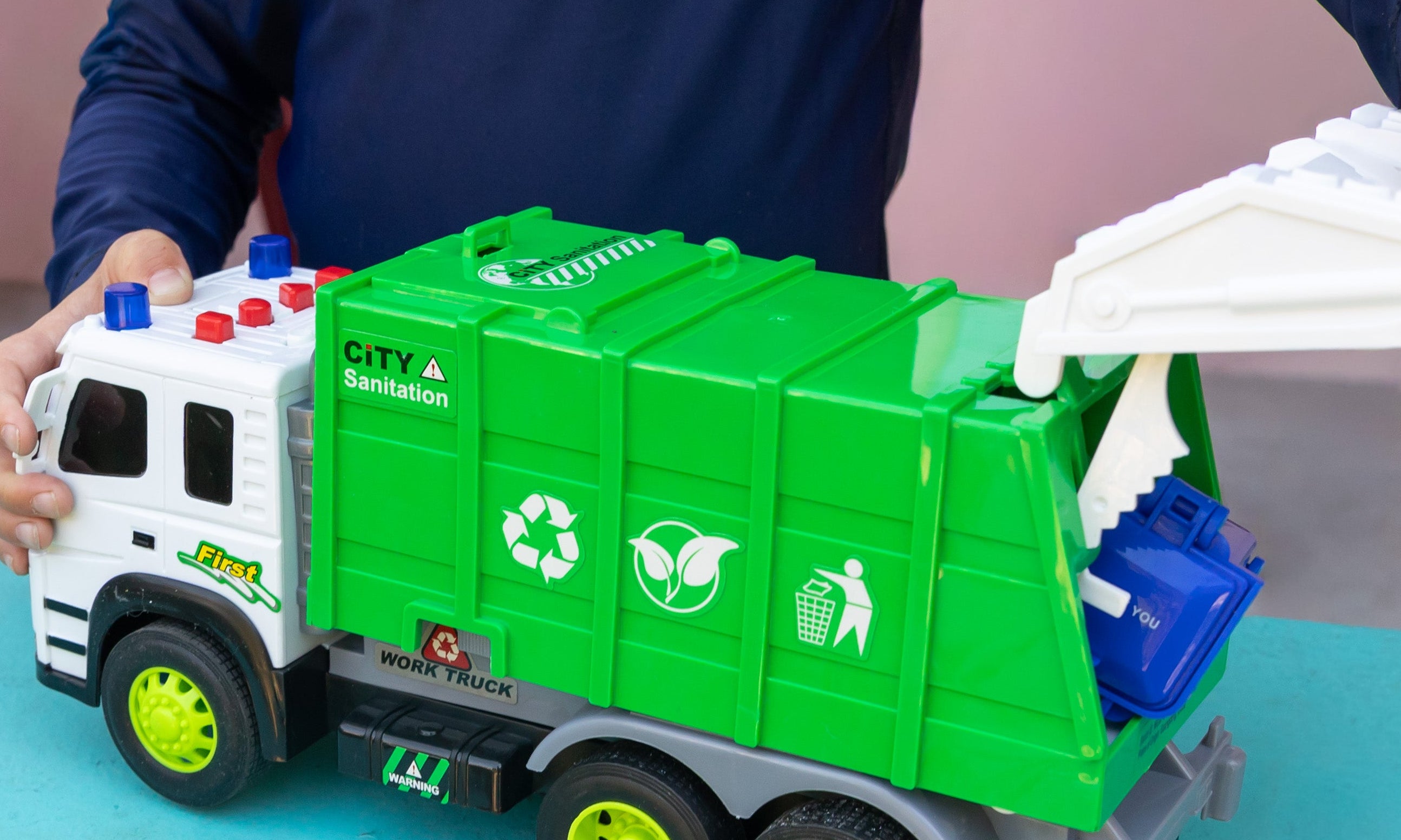 A child's hands and torso are visible as they play with a toy garbage truck. 