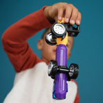 A child holds up a purple toy car pump with a black and yellow pump handle and a small toy car against a solid teal-blue background.