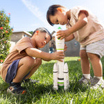 Two children playing with a toy rocketship in a grassy outdoor area.