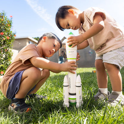 Two children playing with a toy rocketship in a grassy outdoor area.