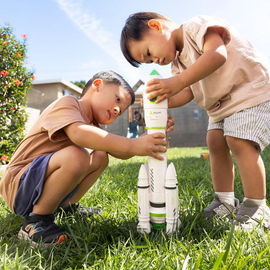 Two children playing with a toy rocketship in a grassy outdoor area.